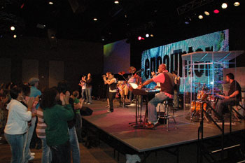 congregation clapping hands with a band performing on stage illuminated by white and red LEDs, screens with lyrics to a song and a LED video wall that says encounter  in the Word of Life Center - Shreveport, Louisiana, USA