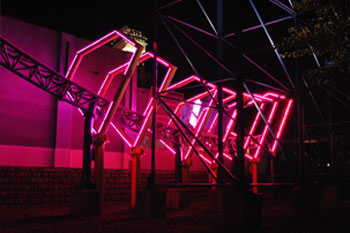 blue rollercoaster tracks going through yellow diamond shaped metal structures with mounted lit LED Pulsar Chromastrip fixtures with vibrant red color on the Bizarro Coaster Thrill Ride at night, Six Flags New England - Agawam, Massachusetts, USA