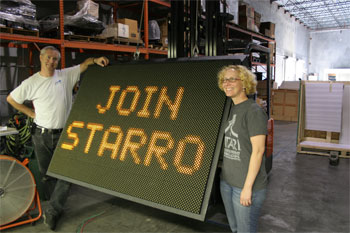 Techni-Lux in-house lighting designer Tony Hansen, and Steffie standing beside large road sign that reads join starro the villian for Justice League: Alien Invasion Warner Bros. Movie World - Gold Coast, Australia