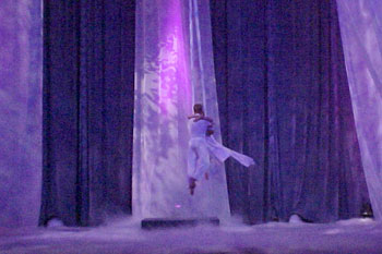 two acrobat performers up in the air on cloth ropes with a purple hues of light all over the stage and low lying fog on the stage floors with abstract gobo patters on the three white curtains Gabriel's Christmas Story, Calvary Orlando, Winter Park, Florida, USA
