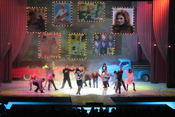 dancers dressed in 1950s era with props of real blue flatbed Ford and red convertible chevy from the 1950s, backdrop red prop curtains downlit accent lights and lit street lights, above the stage many pictures of people in marquee style lit posters on the performers and bright white geometric gobo patterns on the stage floor in the play Glamur, Sexo, Divas y Otras Mentiras - Teatro Nacional, Dominican Republic